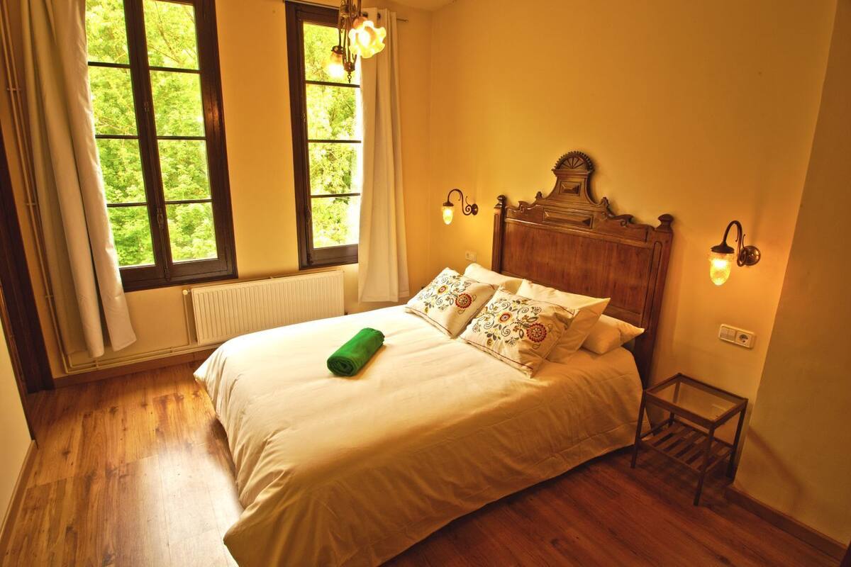 Une chambre avec un lit en bois, un radiateur, une fenêtre avec des rideaux et des lampes fixées au mur.