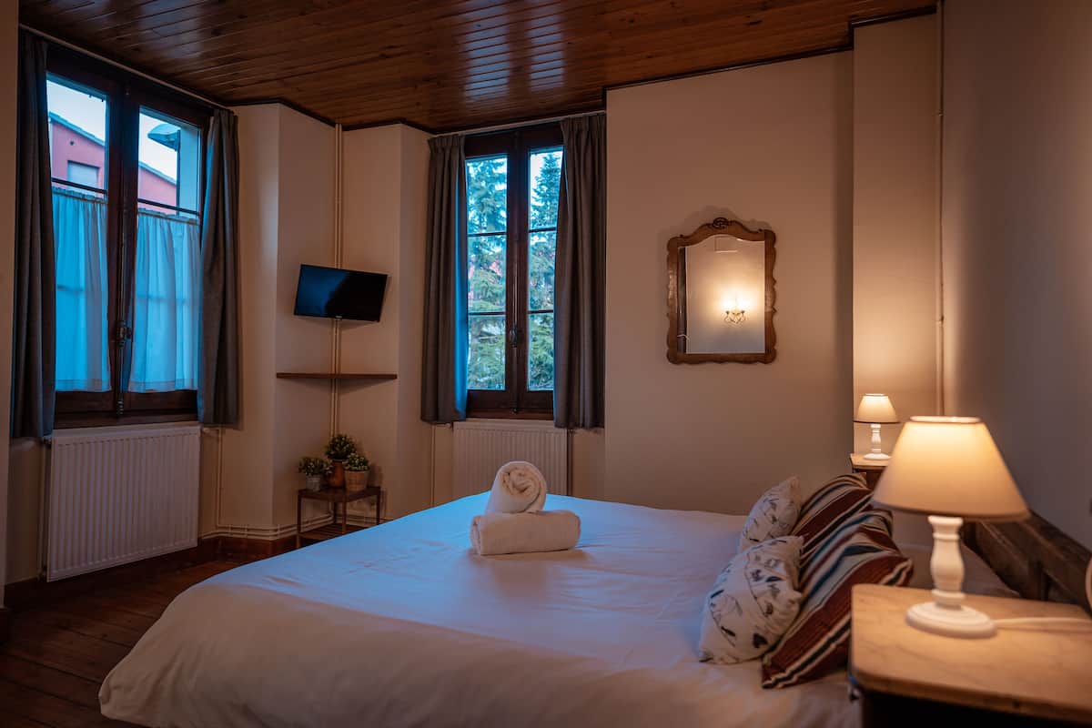 Une chambre à coucher avec un grand lit, un téléviseur fixé au mur, un miroir et deux lampes de chevet.