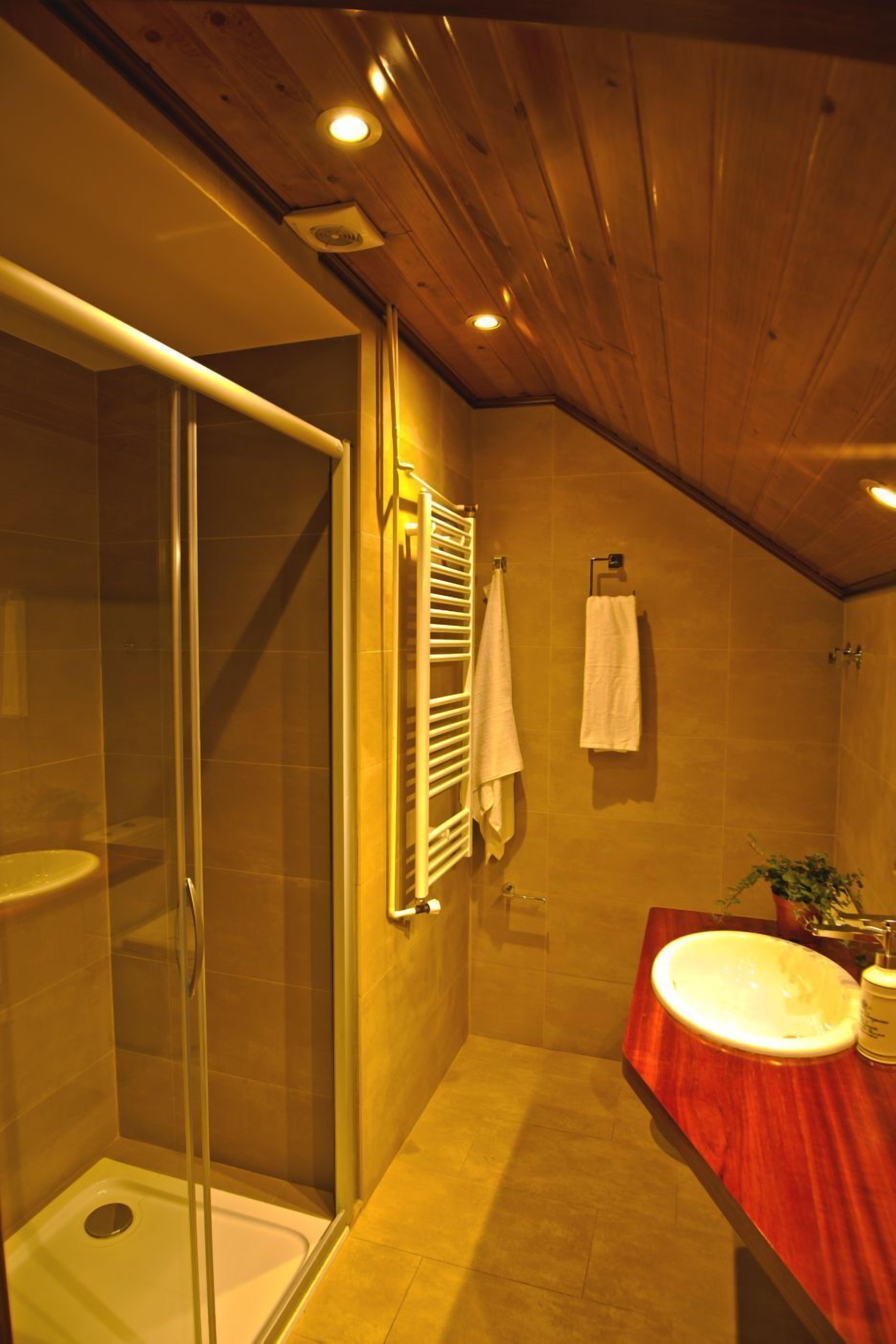 A bathroom with a glass shower enclosure, a wooden vanity with a sink, and two white towels hanging on the wall.
