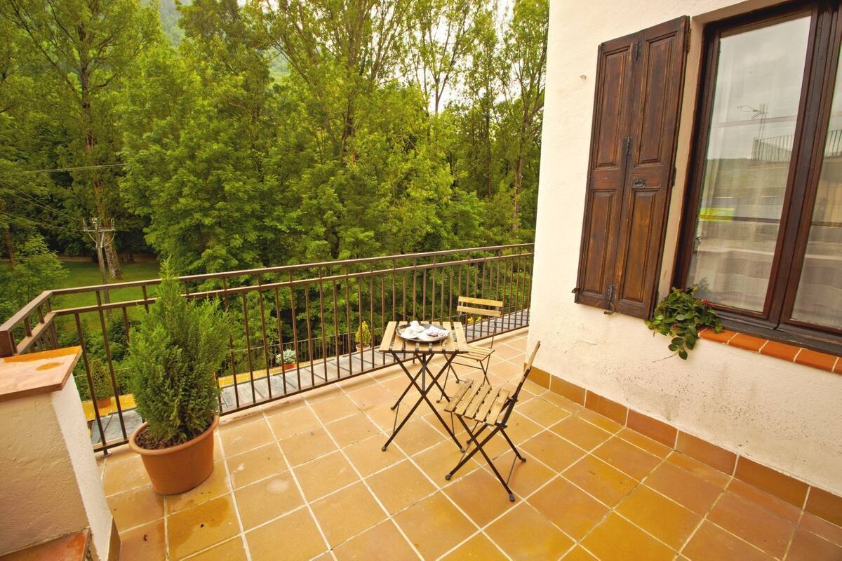 Un balcon agrémenté d’une table et de chaises, entouré d’une rambarde en métal, et offrant une vue sur un espace verdoyant luxuriant.