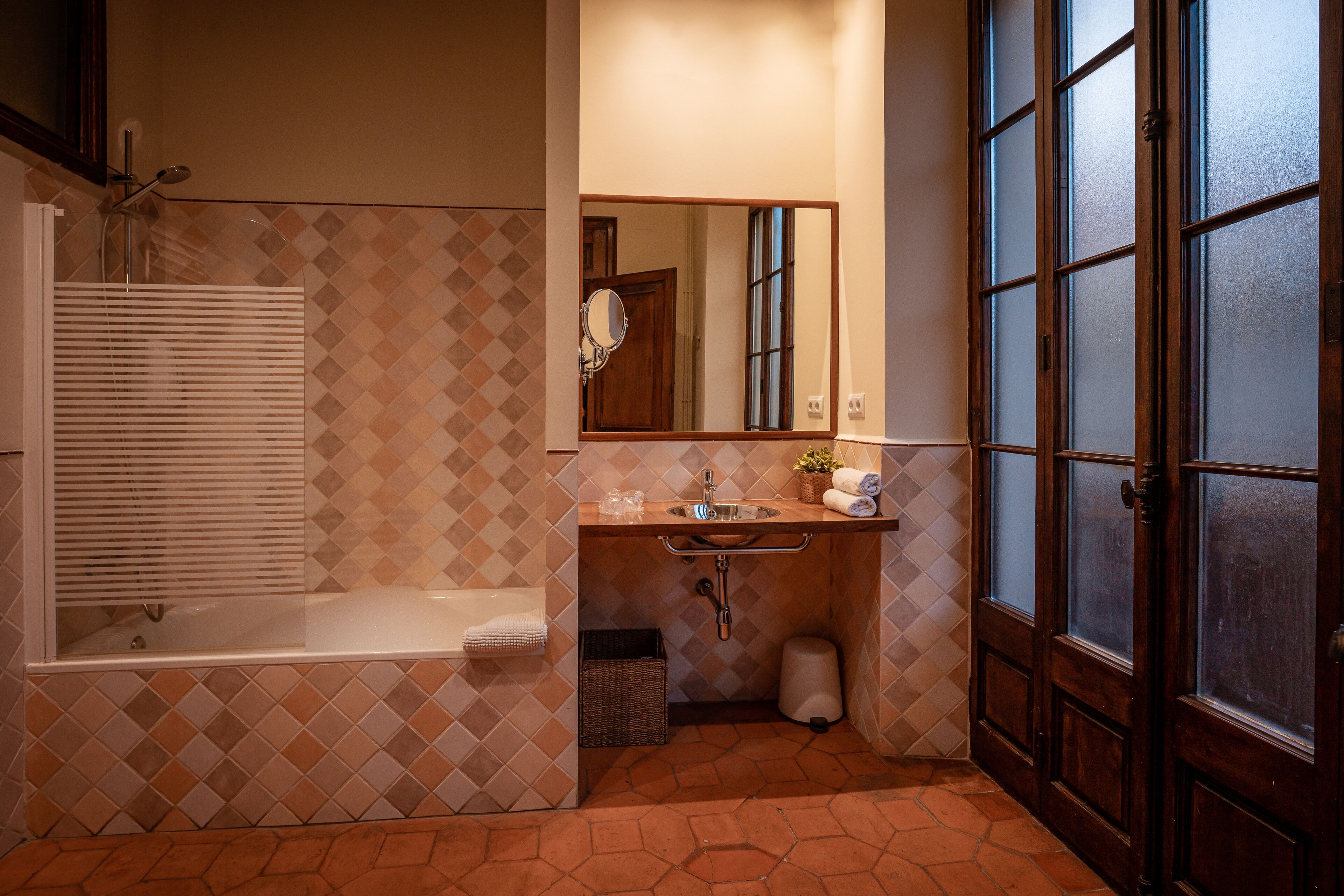 Ein Badezimmer mit Badewanne, Waschbecken, Spiegel und einer Tür mit satinierten Glasfeldern.