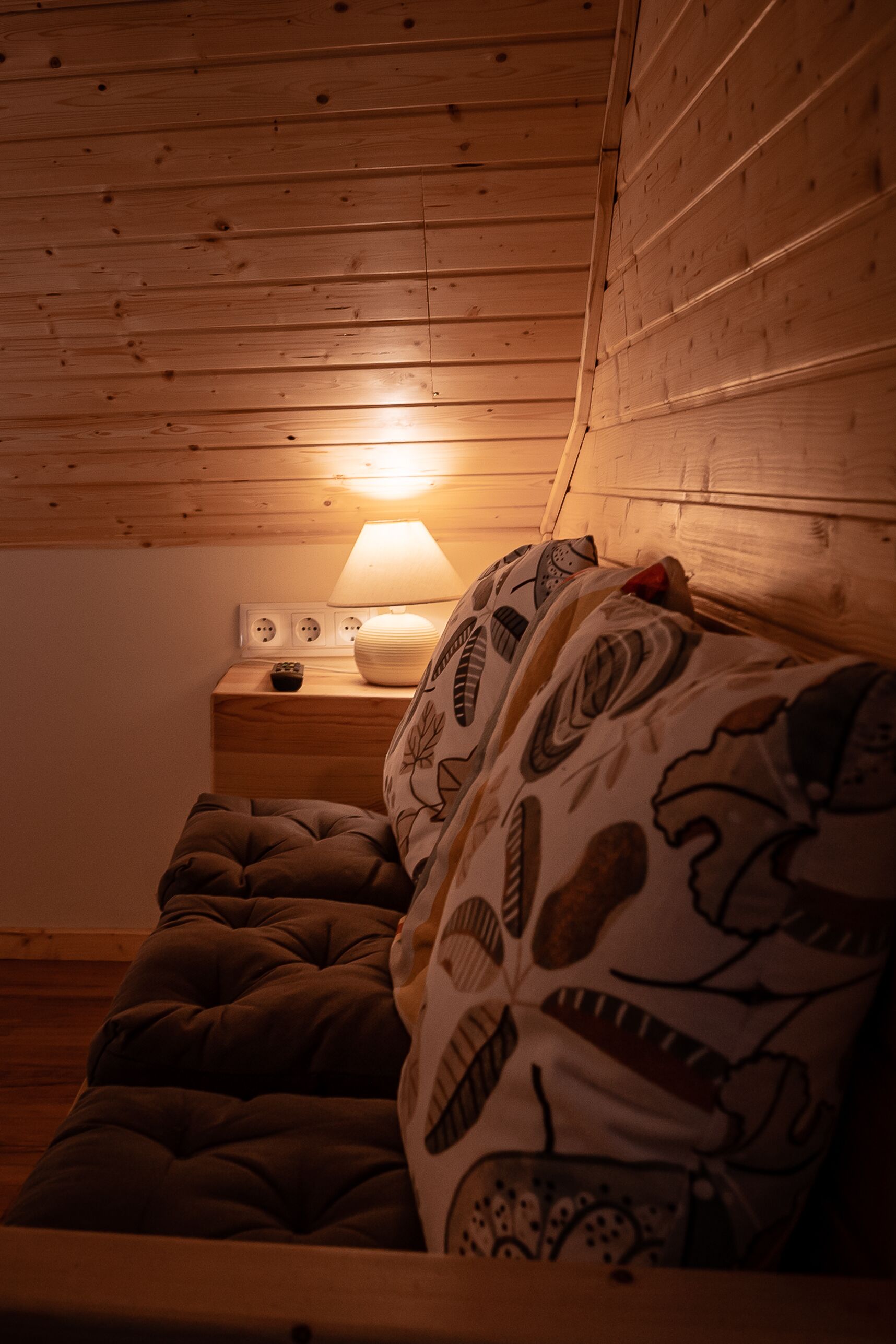 Un dormitorio acogedor con techo de madera, una mesita de noche con lámpara y una cama con ropa de cama estampada.