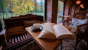 Un banc en bois avec un coussin, une chaise en osier et une table sur laquelle se trouvent un livre ouvert et une tasse.