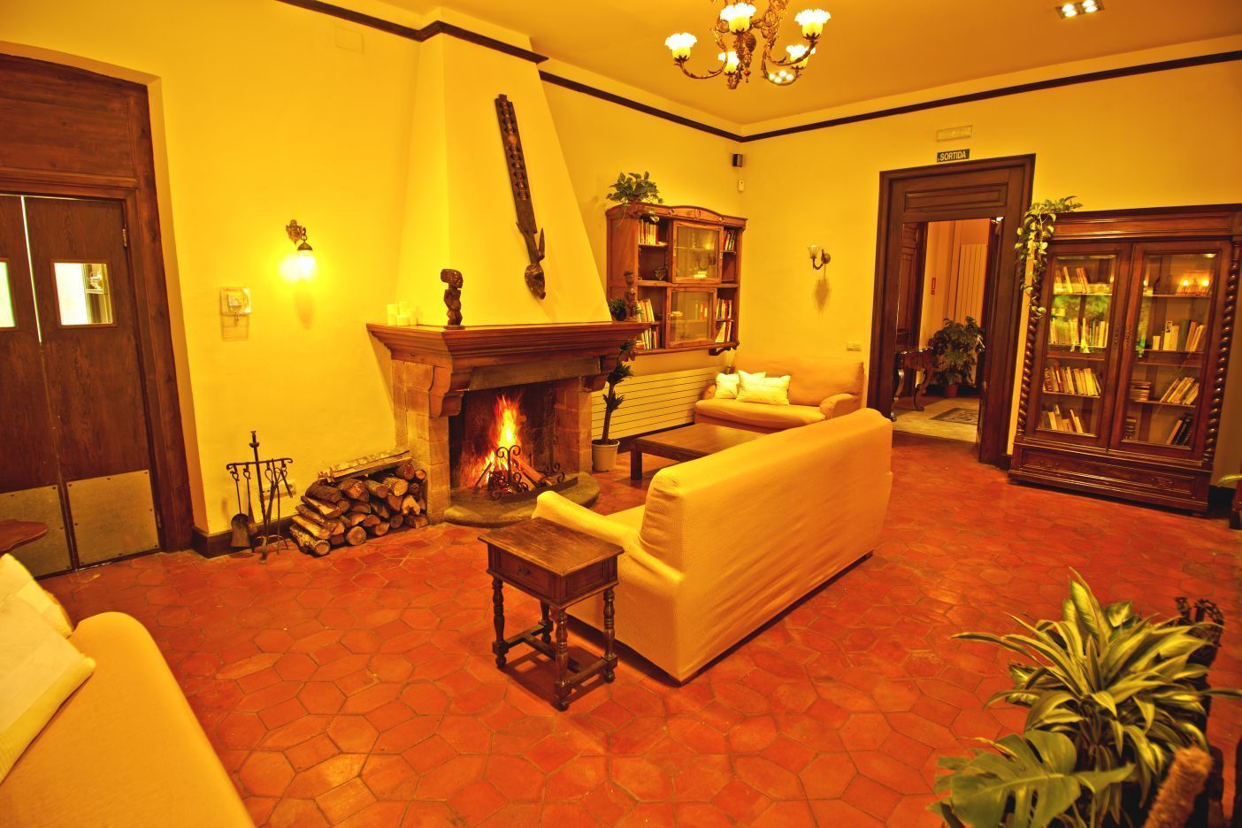 Una sala de estar cálidamente iluminada con chimenea, un sofá, una mesita de centro y una estantería.