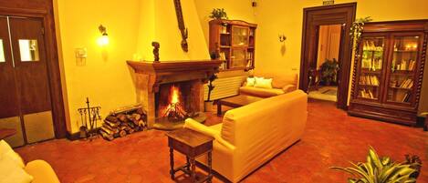 Una sala de estar cálidamente iluminada con chimenea, un sofá, una mesita de centro y una estantería.
