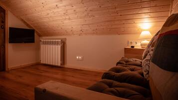 Un dormitorio acogedor en el ático, con techo de madera, una cama, una mesita de noche con una lámpara y un televisor montado en la pared.