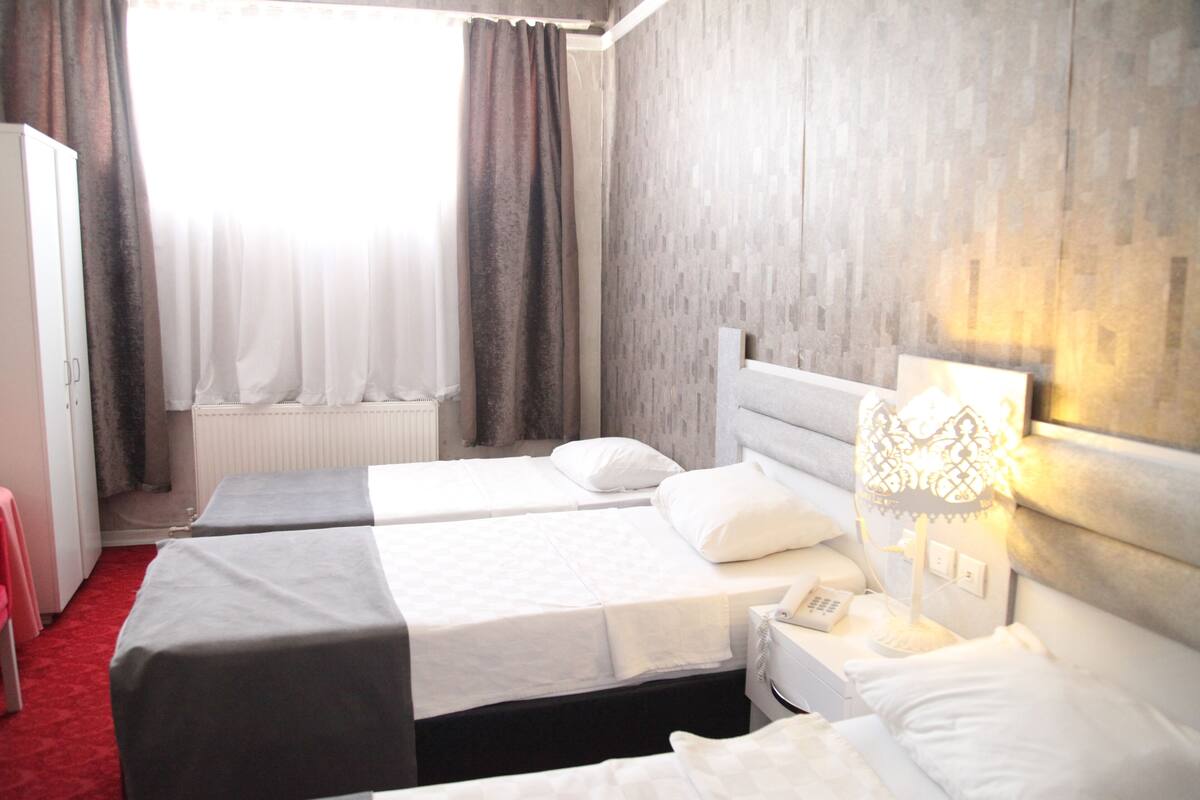 A hotel room with two beds, a radiator, a window with curtains, and a bedside lamp.