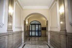 A marble-floored hallway with an arched entrance and a black metal gate. - Domus al Vaticano 36 (Rome)