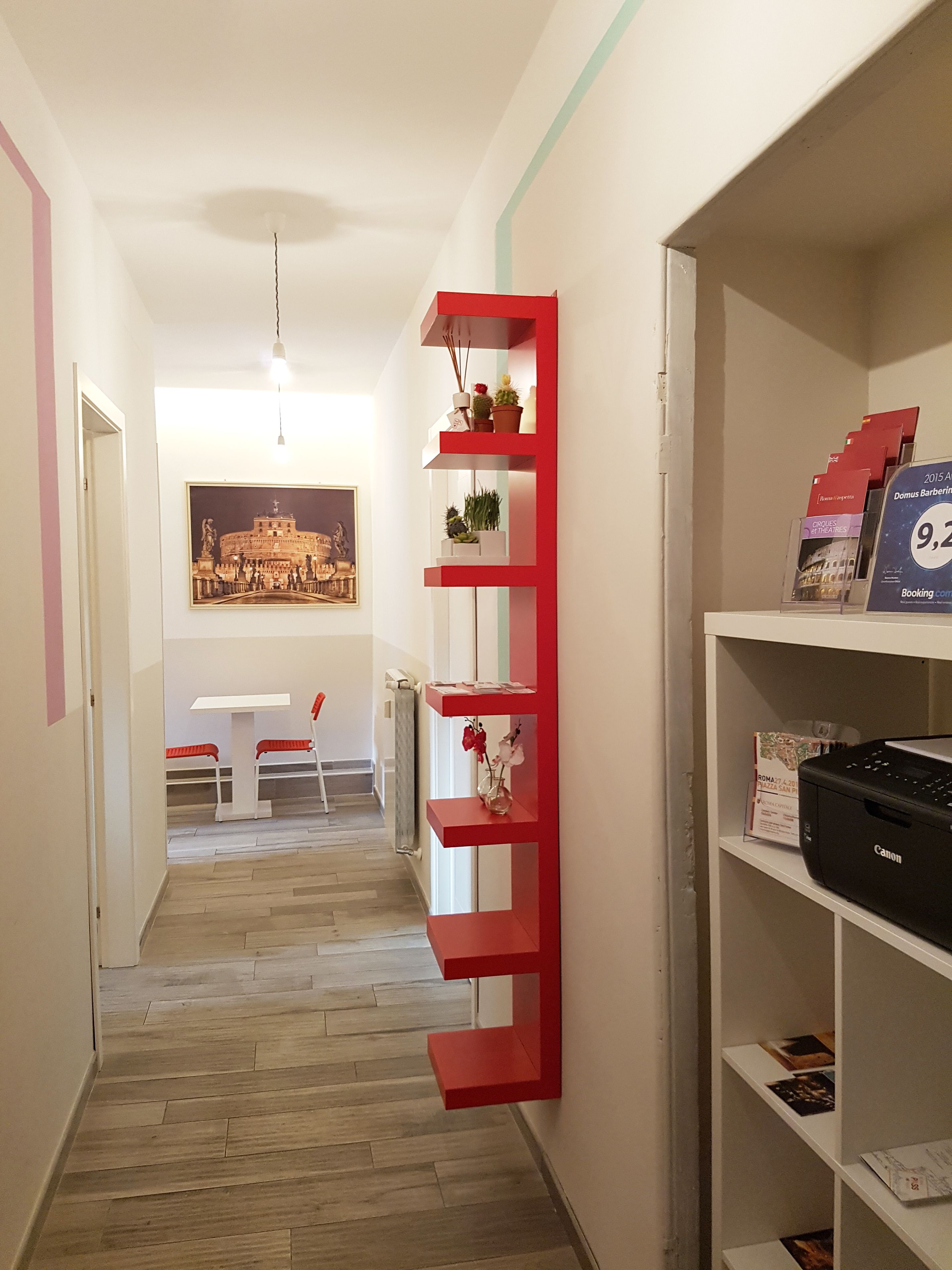 A hallway with a red shelving unit, a framed picture of a building, and a table with chairs.