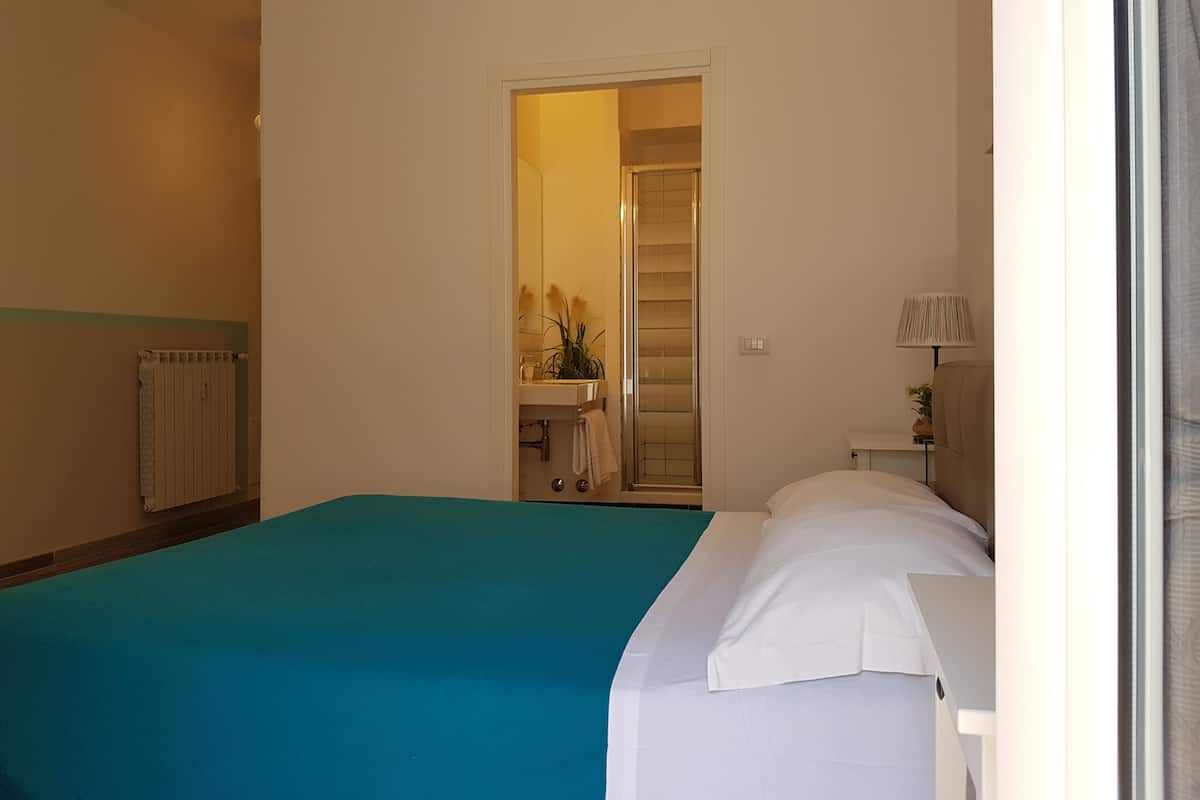 A bedroom with a bed, a bathroom with a shower, and a hallway leading to a staircase.
