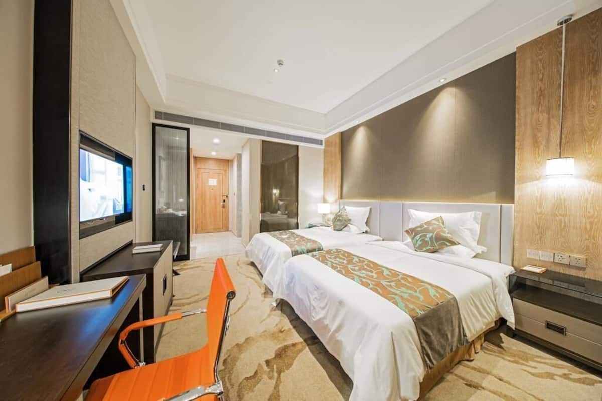A hotel room with two beds, a desk, a TV, and a seating area.