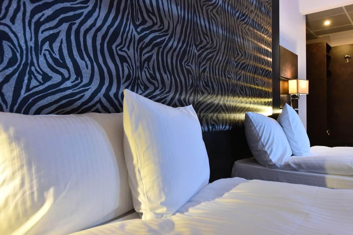 A hotel room with a zebra-striped headboard, a bed with white linens, and a bedside lamp.