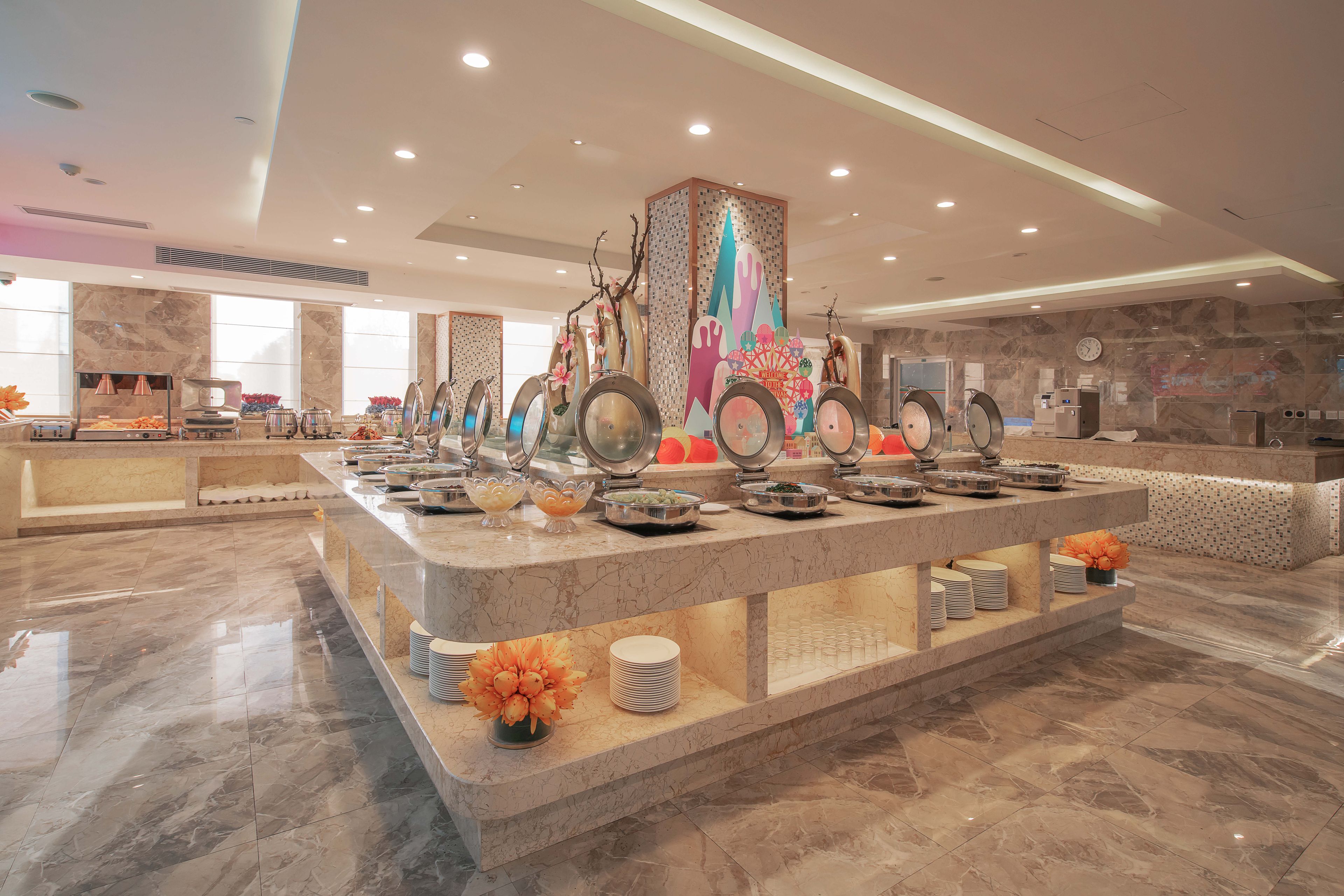 A well-lit, spacious hotel lobby with a marble reception desk, a large decorative column, and a clean, modern design.