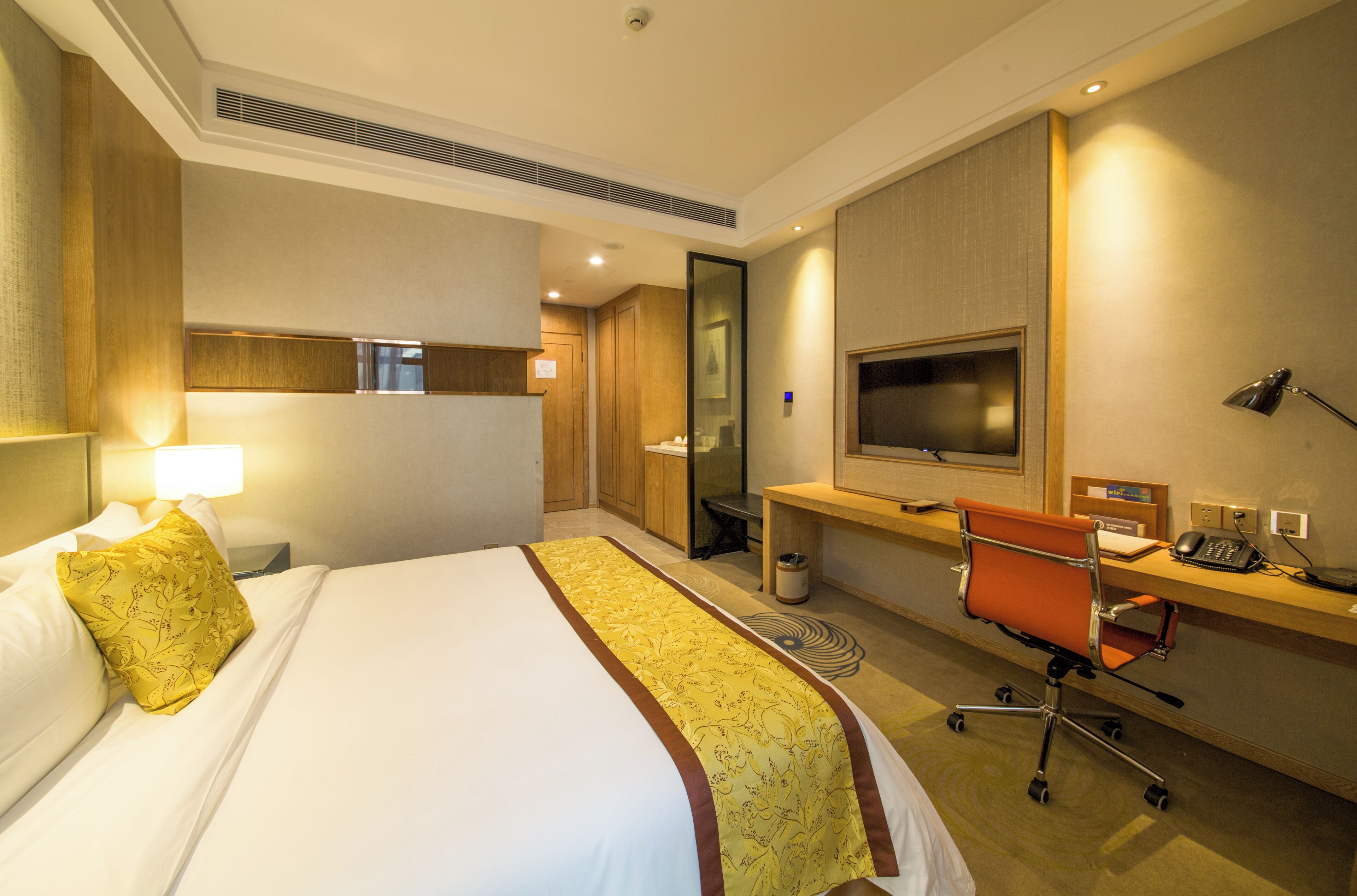 A hotel room with a bed, desk, chair, TV, and a mirror.