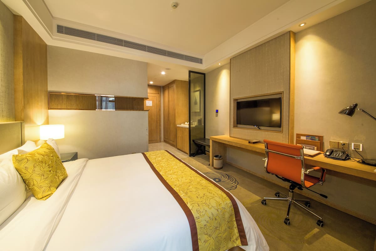 A hotel room with a bed, desk, chair, TV, and a mirror.
