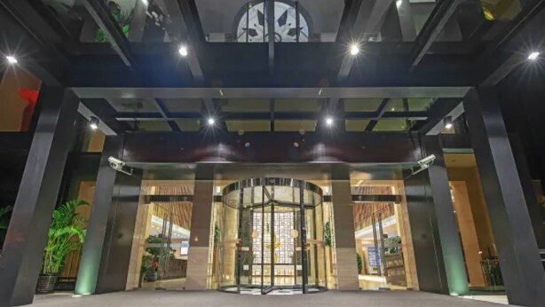 Una entrada de hotel moderna con puerta giratoria, grandes ventanales y un techo con tragaluz circular.