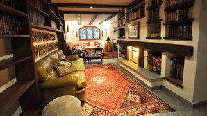 Ein gemütliches Wohnzimmer mit Kamin, Bücherregalen, einem Ledersofa und einem gemusterten Teppich.