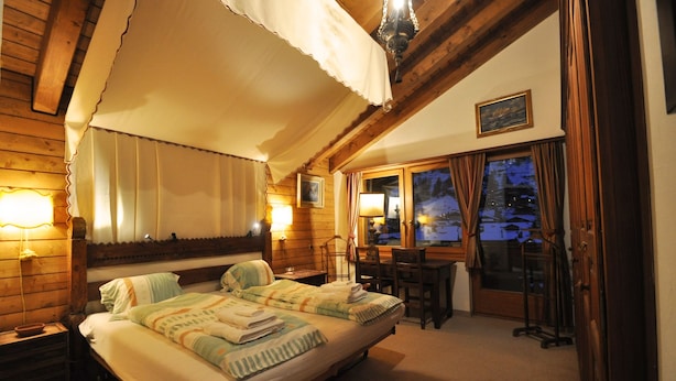 Ein gemütliches Zimmer mit Bett, Tisch und Stühlen. Ein Fenster mit Vorhängen bietet einen Blick nach draußen.