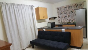 A compact kitchen with a wooden cabinet, a black countertop, a small black sofa, and a curtain. - Indigo Guesthouse (Pinetown)