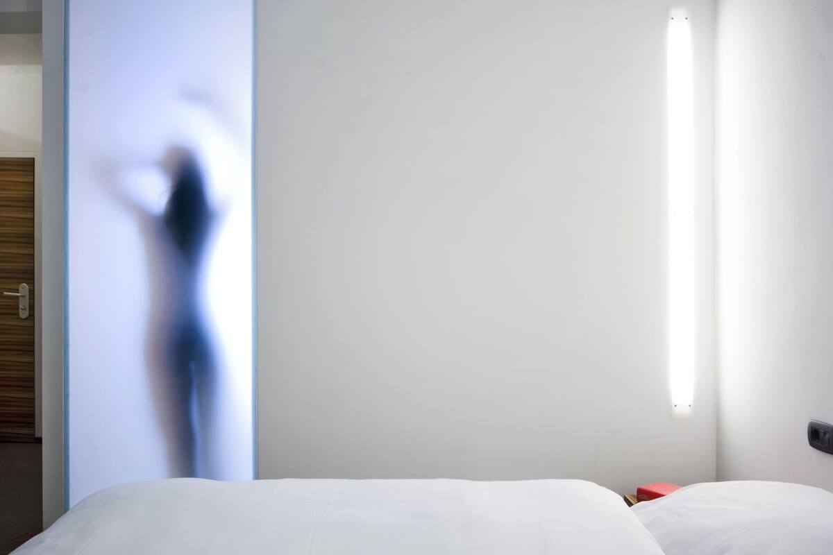A hotel room with a bed, a nightstand, and a wall-mounted light fixture.