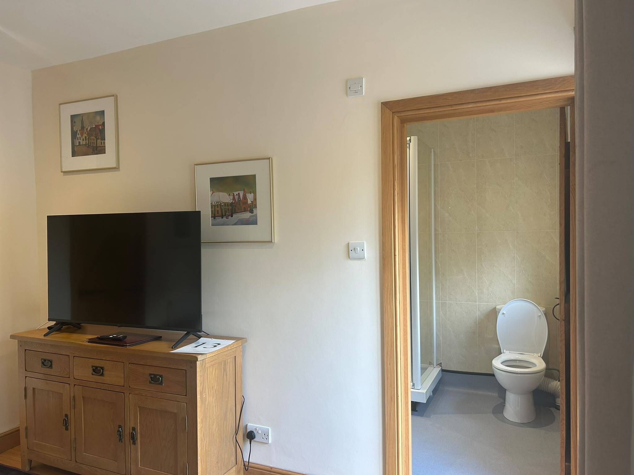 A room with a television on a wooden cabinet, a door leading to a bathroom, and two framed pictures on the wall.