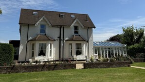 A two-story house with a conservatory, a brick wall in front, and a well-maintained lawn. - Hookwood Lodge (Horley)