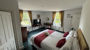 A hotel room with a bed, a desk, a chair, a television, and two windows with curtains. - Hookwood Lodge (Horley)