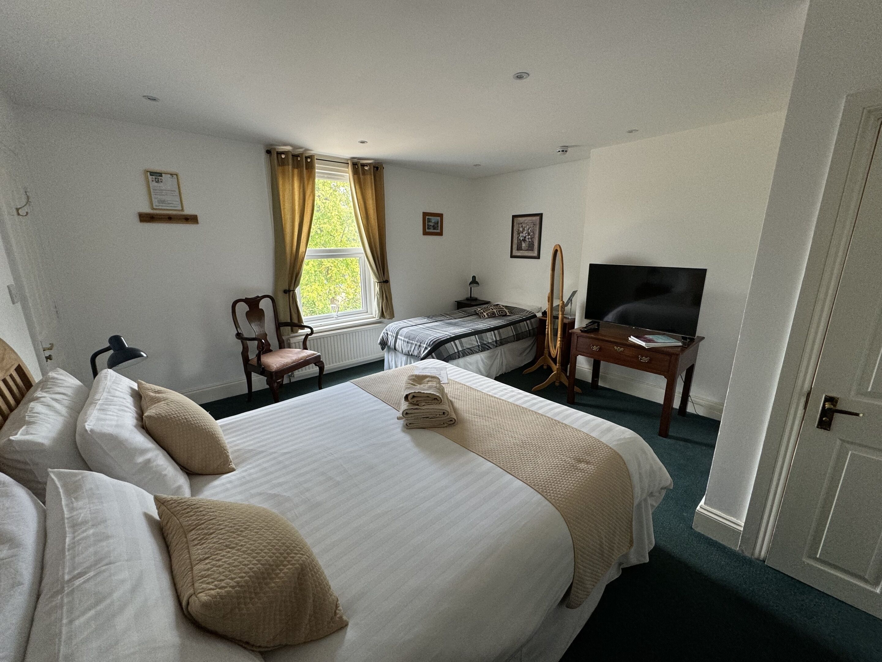 A hotel room with two beds, a desk, a chair, a television, and a window with curtains.