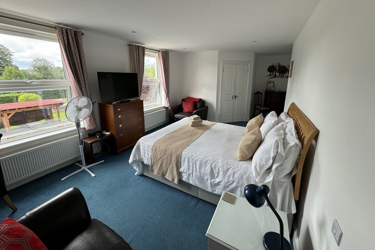 A hotel room with a bed, a desk, a chair, a dresser, a television, a window with curtains, and a view of the outside.