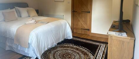 A bedroom with a bed, a wooden door, a television, and a small rug.