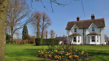 Stunning two-story house with a traditional design, featuring a pitched roof and a chimney, set amidst a beautifully manicured lawn and lush gardens.