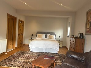 A bedroom with a bed, bedside tables, a dresser, a patterned rug, and a leather sofa. - Hookwood Lodge (Horley)