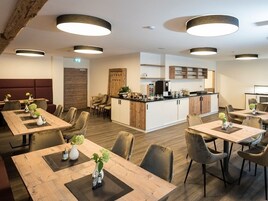 A modern dining area with wooden tables and chairs, a central kitchen island, and pendant lighting.