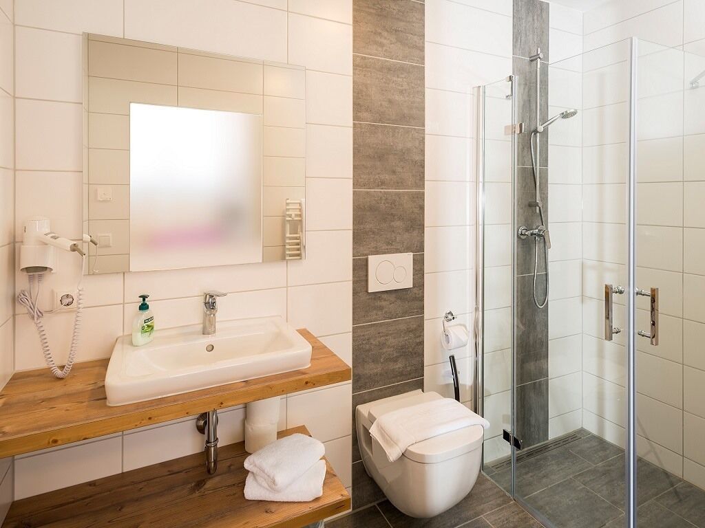 Un baño moderno con tocador de madera, un espejo grande, ducha con puerta de vidrio y un inodoro.
