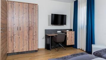 Une chambre d’hôtel avec une armoire en bois, un bureau avec une chaise, un téléviseur fixé au mur et un lit avec une literie à motifs.