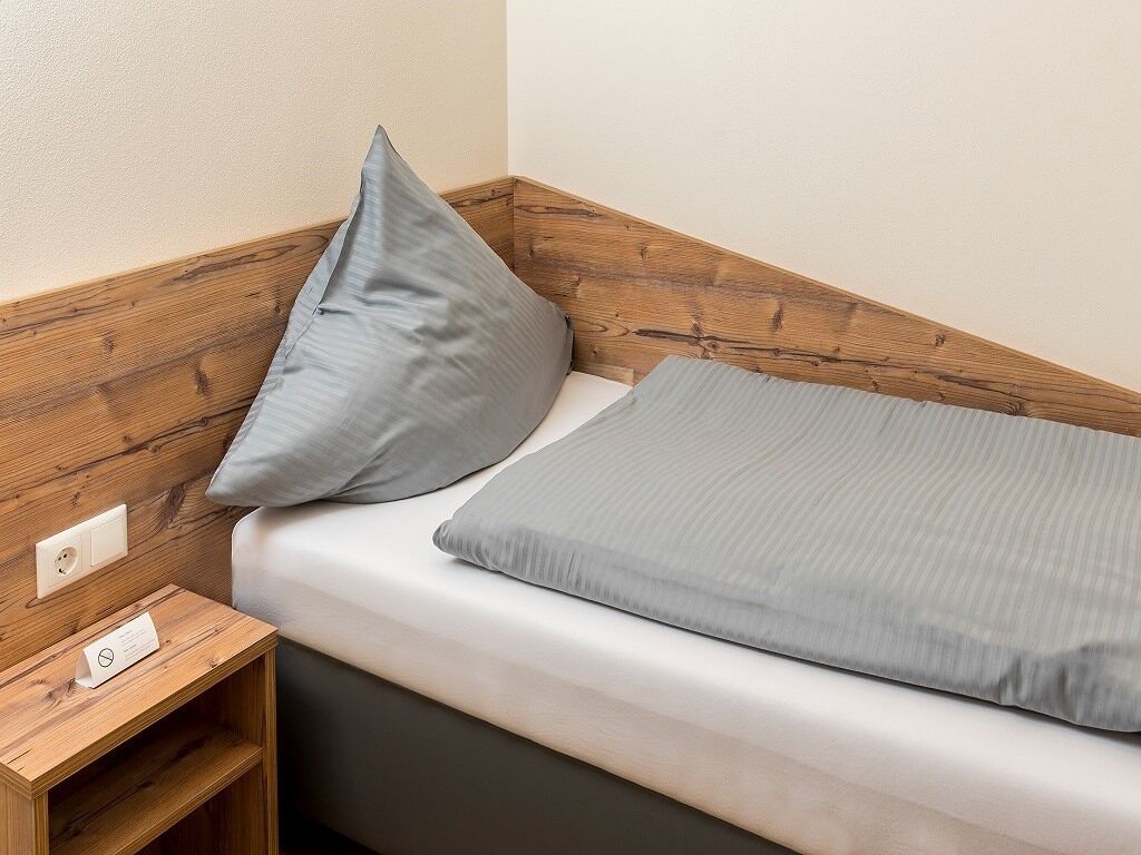 Ein kleines Bett mit Holz Kopfteil, einem Nachttisch und einem grauen Kissen.