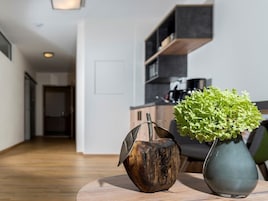 A modern living room with a wooden floor, a round coffee table, a decorative wooden sculpture, and a green plant in a vase.