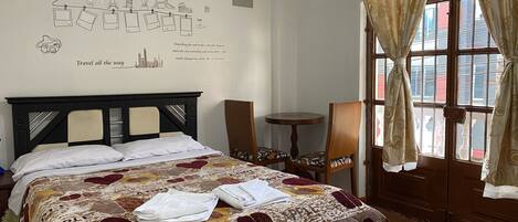 Habitación de hotel con cama, una mesita, una silla y ventana con cortinas.