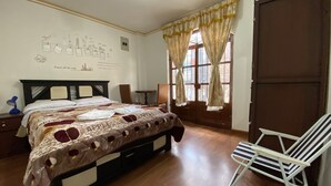 Habitación de hotel con cama, una silla, un escritorio, una pared con un mural de la ciudad y una ventana con cortinas.