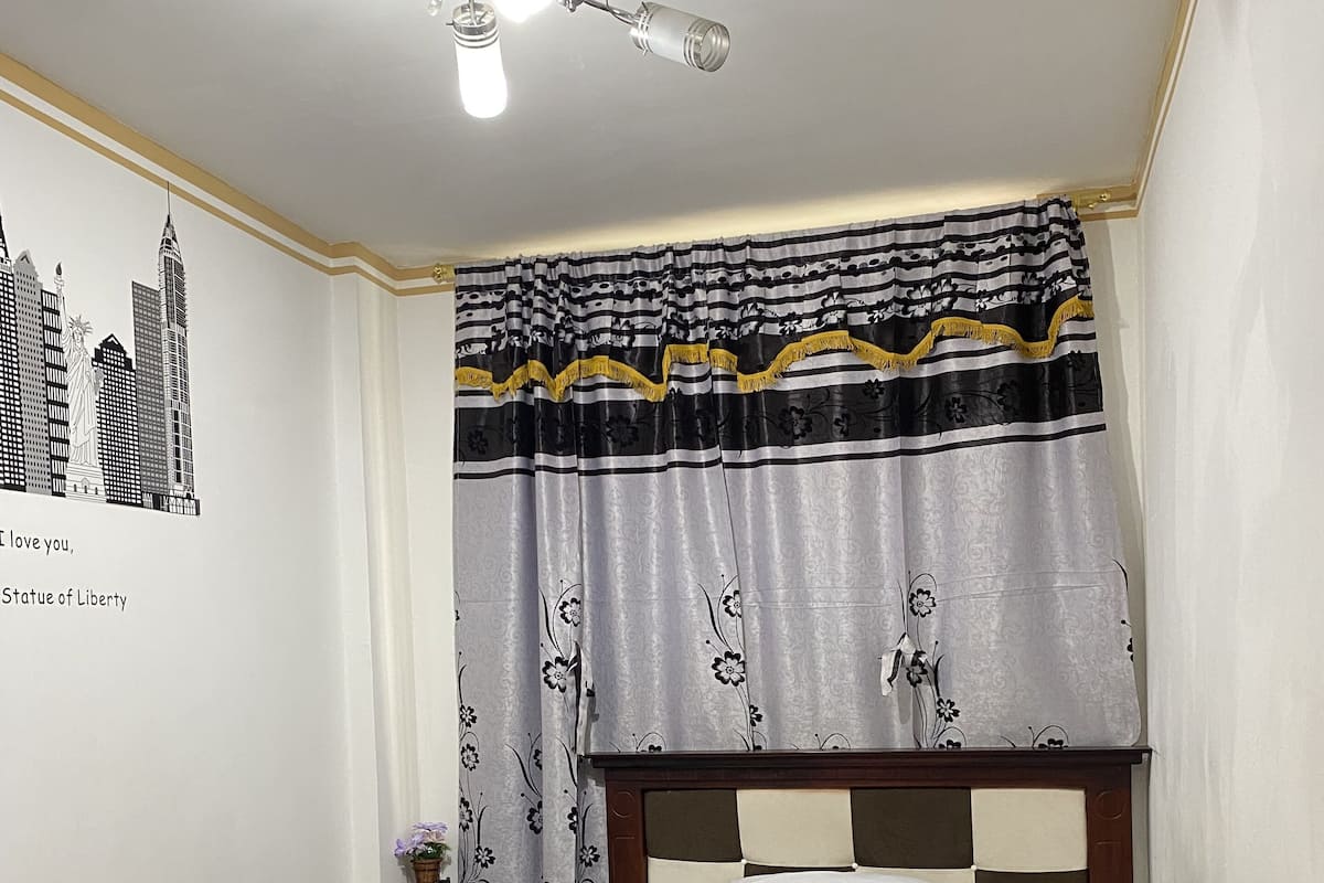 A bedroom with a bed, a nightstand, a lamp, and a wall decoration of the Statue of Liberty.