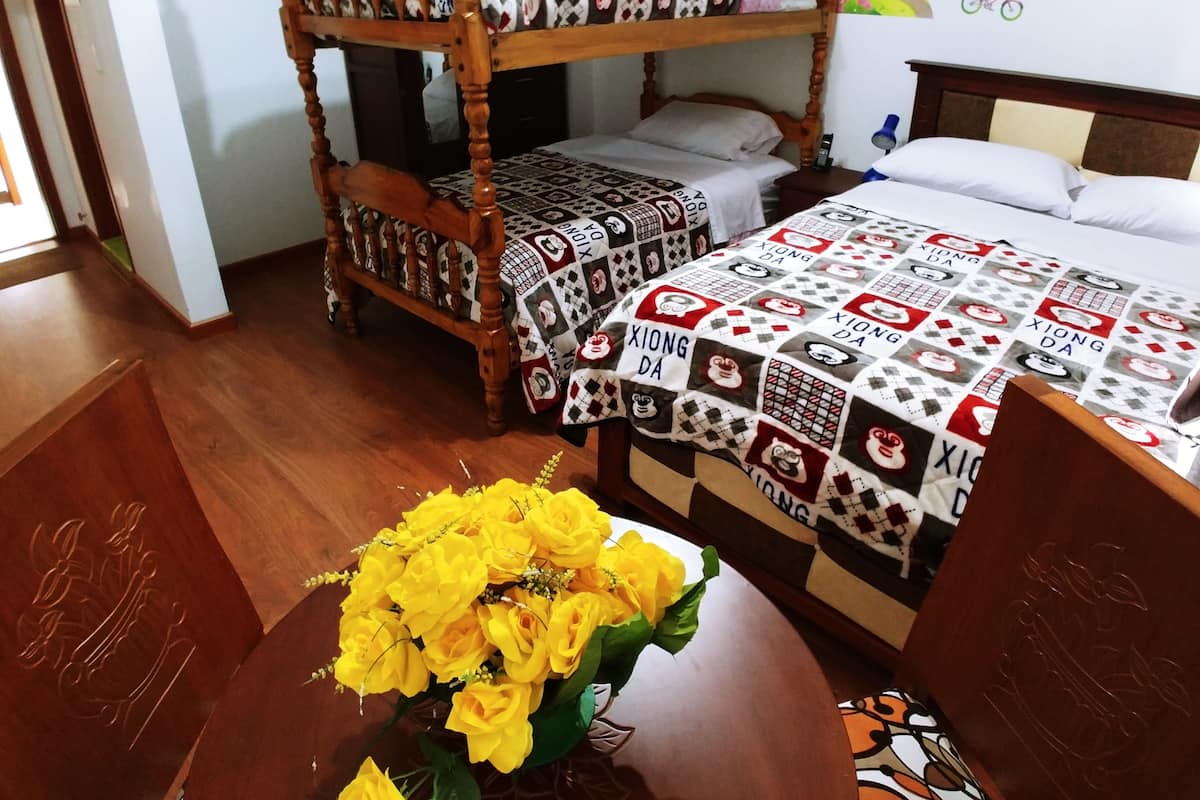 A room with a bunk bed and a single bed, both with patterned bedding. There is a wooden table with a vase of yellow flowers.