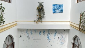 Una habitación acogedora con piso de césped artificial verde, sofás blancos con cojines verdes, una mesita redonda con un jarrón de flores y una mesa de centro negra.