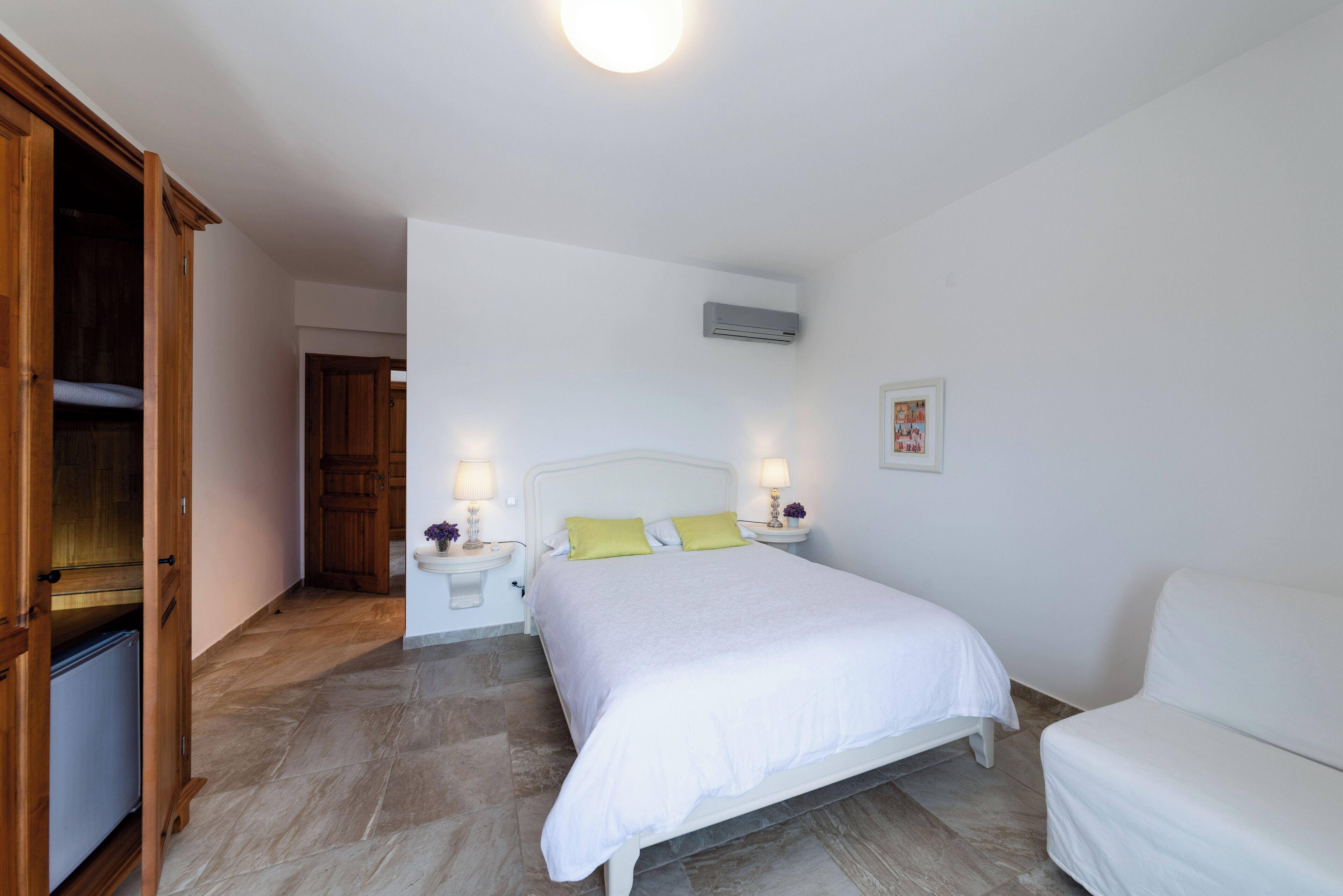 Une chambre à coucher comprenant un lit, des tables de chevet, une armoire et un appareil de climatisation.