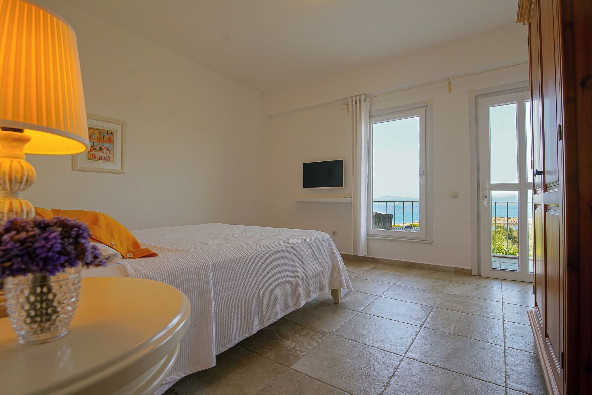 Un dormitorio con cama, televisor en la pared, ventana y vista al mar.