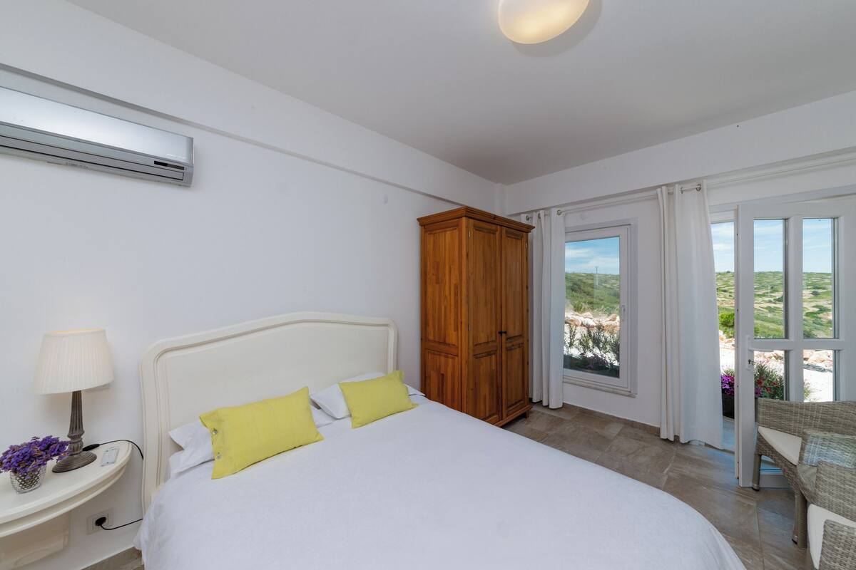 A bedroom with a bed, a nightstand, a wooden wardrobe, and a view through a glass door.