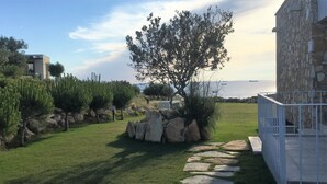 Un edificio de piedra con un camino de piedra que lleva a una zona cubierta de césped, árboles y vistas al mar.