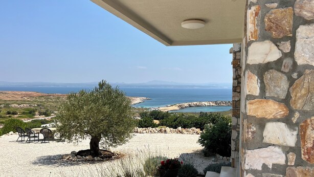 Un muro de piedra, un árbol y vistas al mar y las montañas.