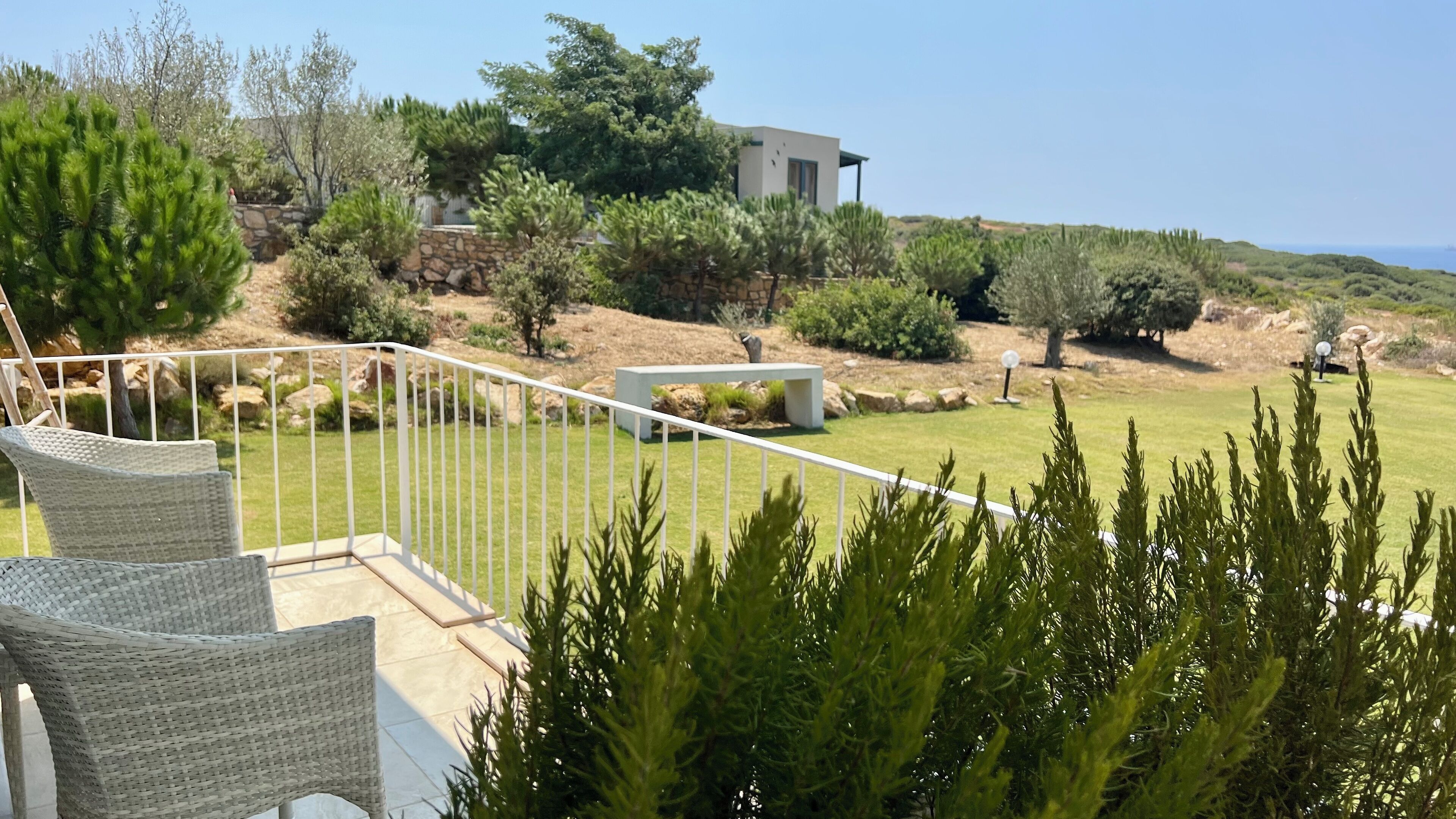 Un patio con sillas de mimbre, un muro de piedra y vistas a un edificio moderno y un paisaje natural.