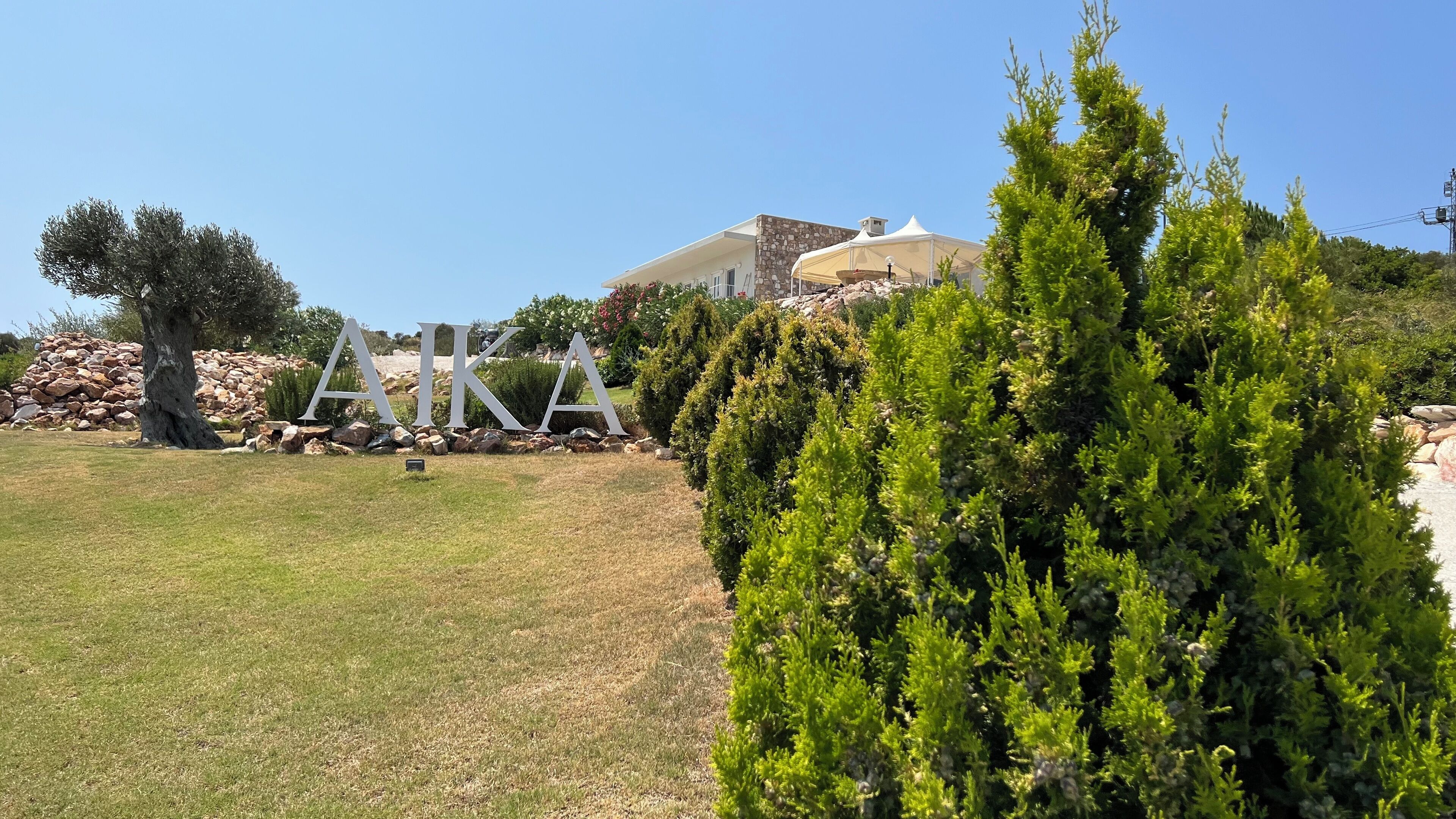 A landscaped area with a large 'AKA' sign, a stone wall, and a building with a white facade.