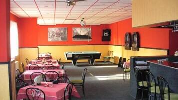 Un restaurante con paredes rojas y amarillas, varias mesas con manteles rosa y una mesa de billar en el centro.
